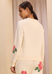 Back view of a woman wearing a cream-colored sweatshirt with floral embroidery on the sleeves, paired with matching pants, showcasing a comfortable and stylish casual outfit.