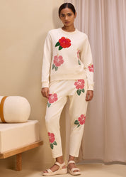 Full view of a woman wearing a cream-colored sweatshirt and pants set with bright floral embroidery, showcasing a comfortable and stylish casual outfit.